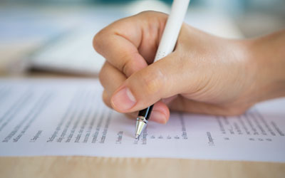Foto de una mano sosteniendo un lapicero rellenando un formulario